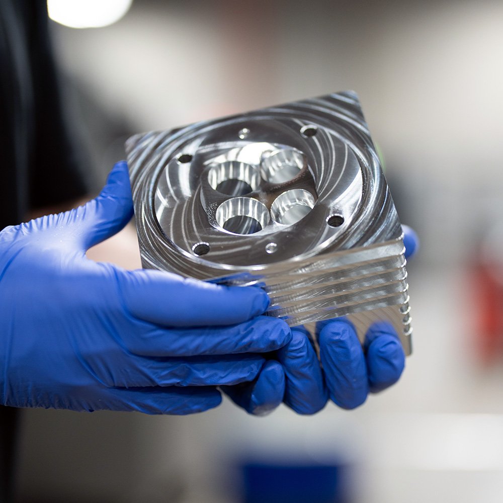 Gloved hands holding a precision-machined metal part